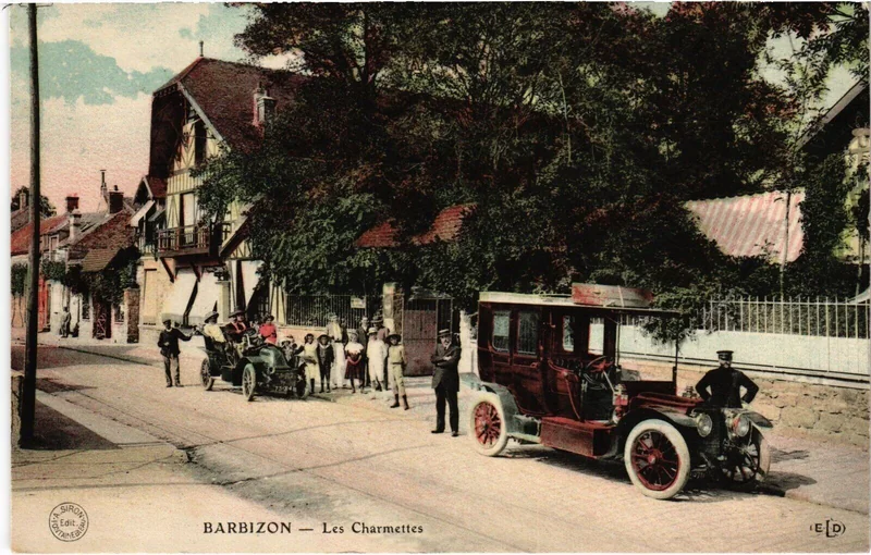 Carte postale colorisée des Charmettes vers 1910 : façade à colombages sur la Grande Rue, deux automobiles d'époque et un groupe d'habitants devant le portail.